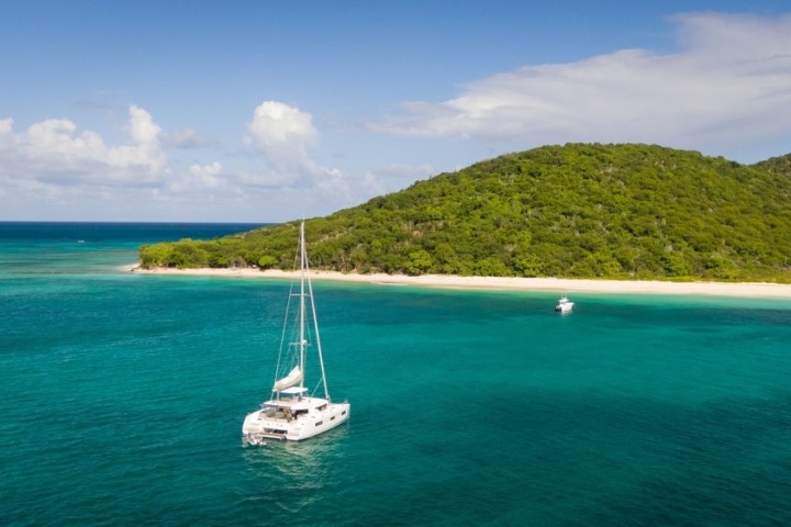 Catamaran sailing near a lush green island with clear turquoise waters and a sandy beach.