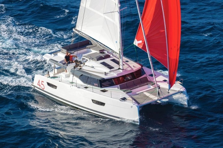 A sailboat with white and red sails navigating blue ocean waters.