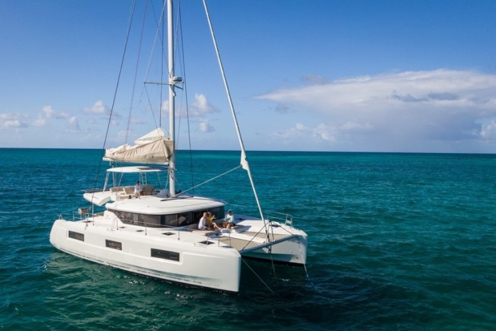 A white catamaran sailboat on turquoise ocean under blue sky with scattered clouds.