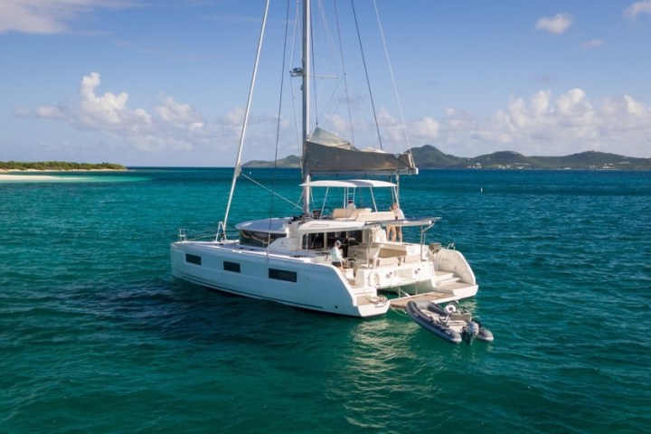 Sailing catamaran anchored in clear turquoise water with distant islands and a blue sky.