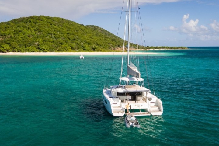 Catamaran in clear turquoise water near a lush green island and sandy beach.
