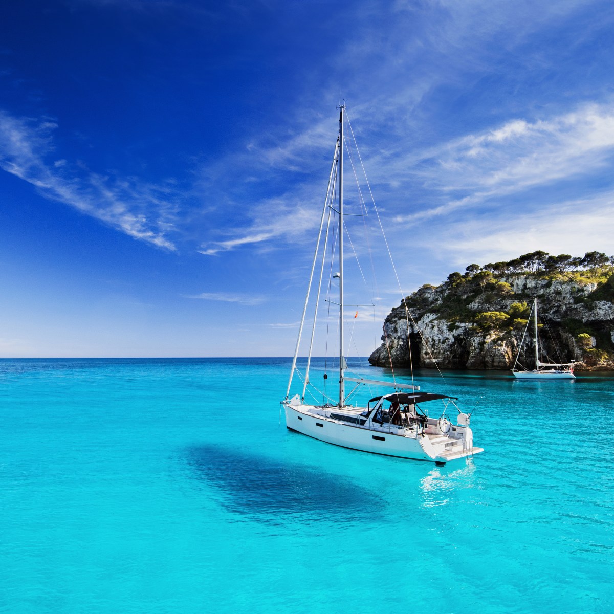 Sailboat on clear turquoise water near rocky cliffs under a bright blue sky.