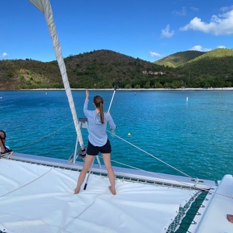 Three people on a catamaran overlooking a bay with hills and blue sky.